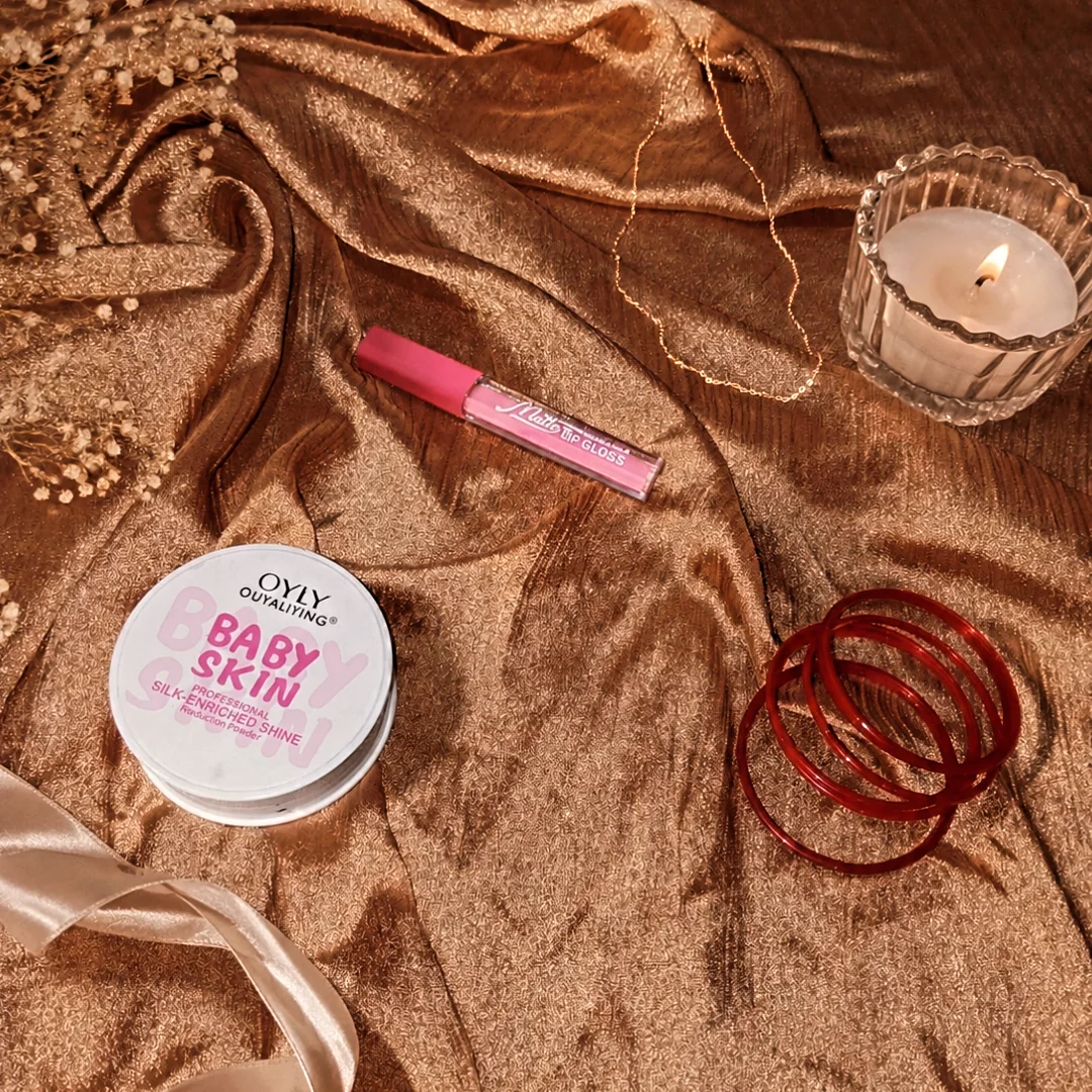 Lip gloss and beauty products on gold fabric with candle